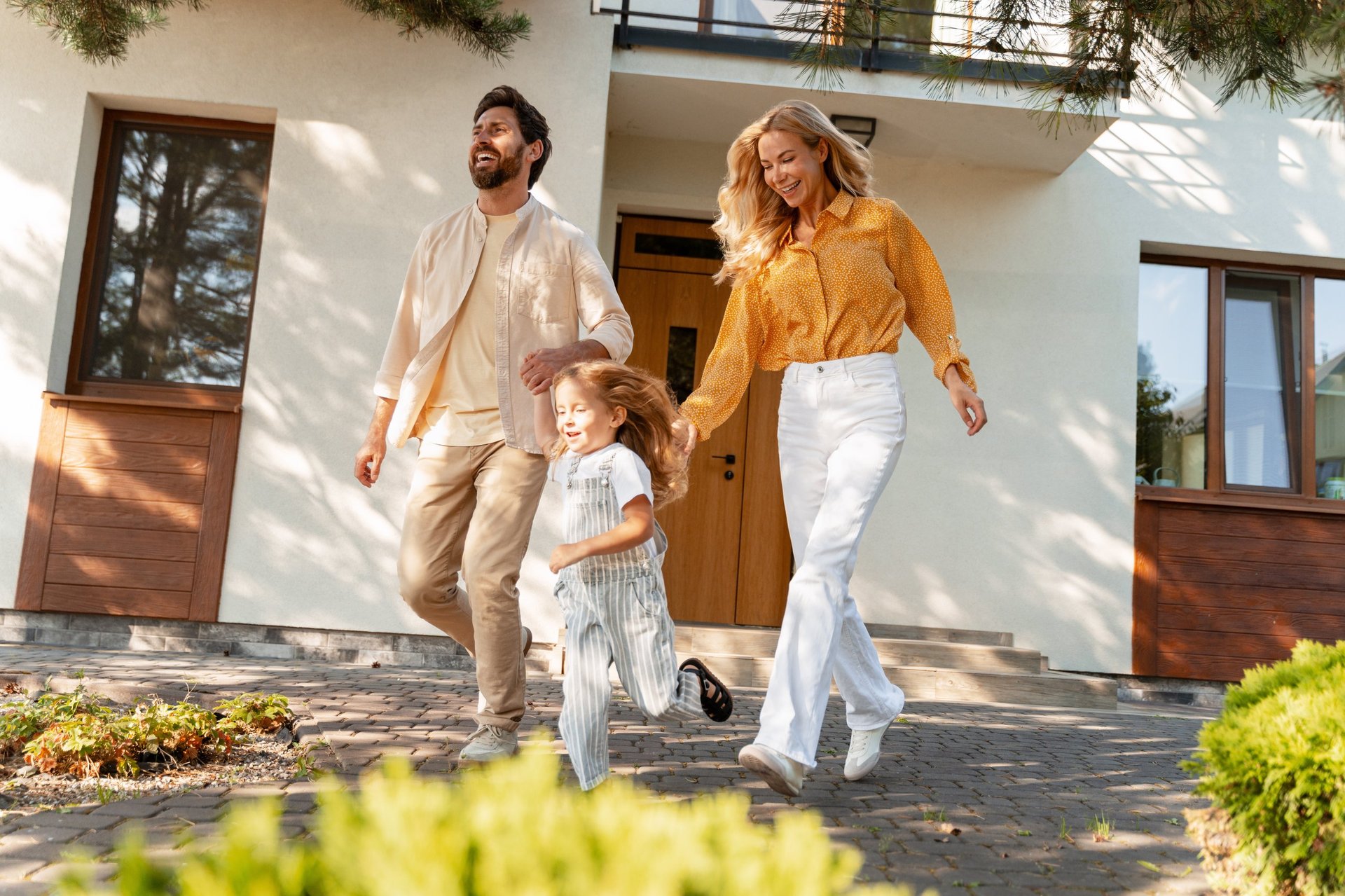 Parents and their college-aged daughter leaving a modern house together on a sunny day